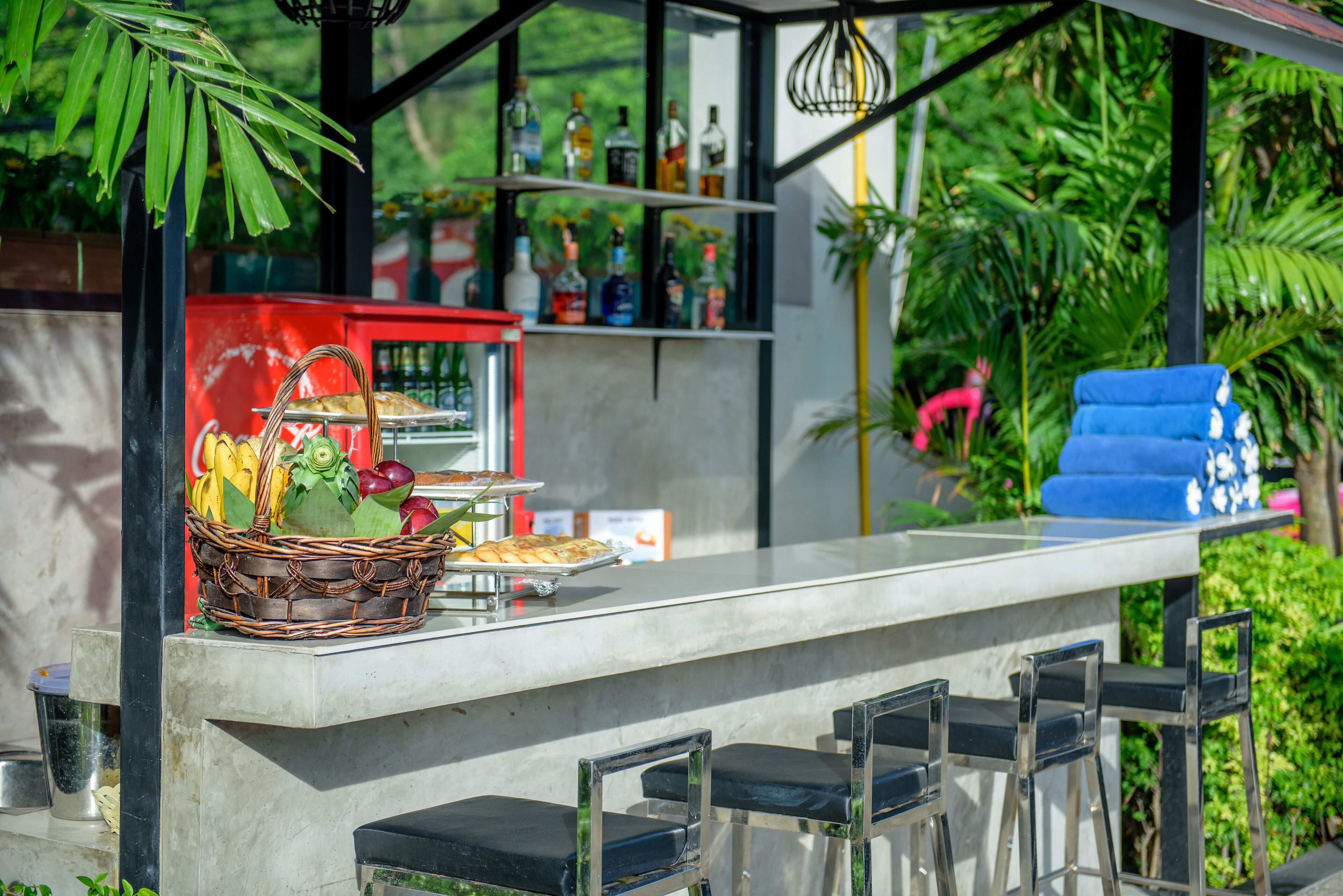 An outdoor bar area with a concrete counter, wicker basket with fruits, and a selection of bottles on shelves.