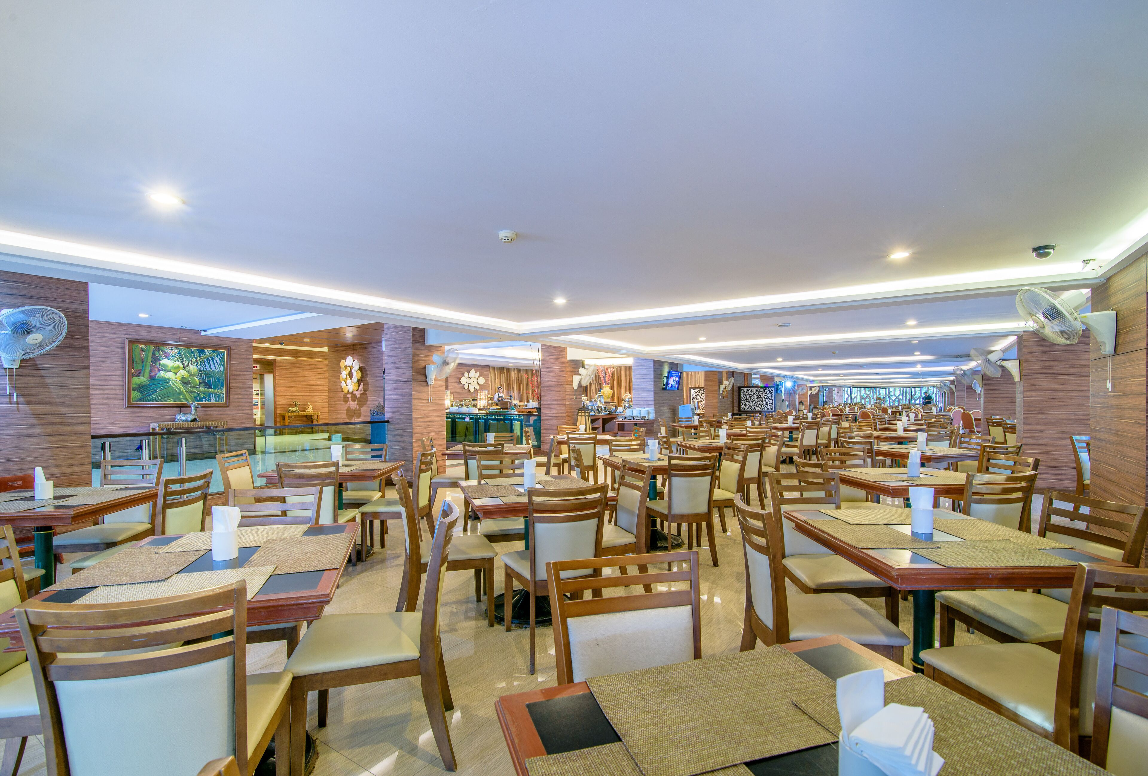 Um restaurante amplo com várias mesas e cadeiras, uma área de balcão e uma tela de televisão.