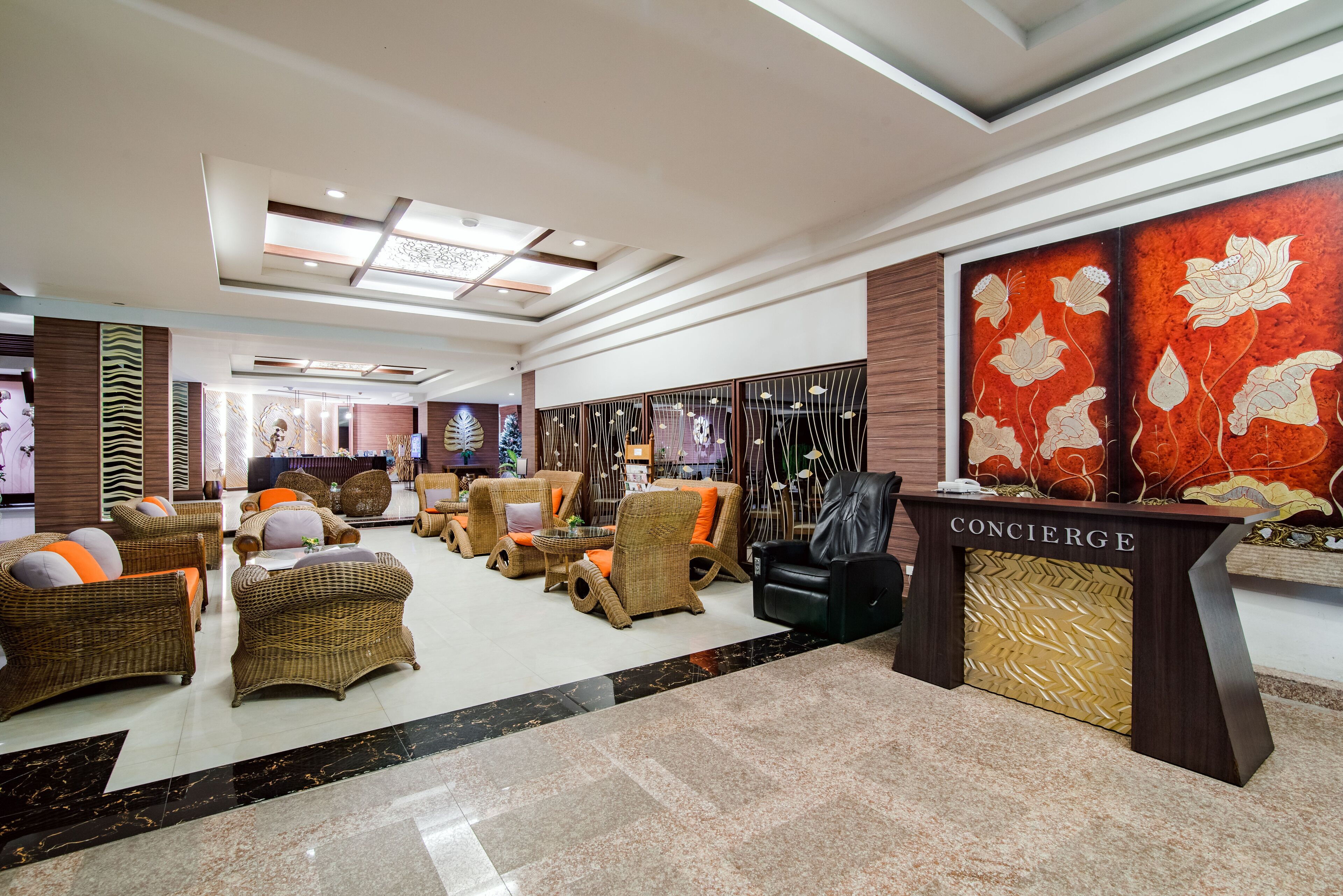 Un hall con mobiliario de mimbre, un mostrador de recepción con la etiqueta 'CONCIERGE' y una gran obra de arte floral en la pared.