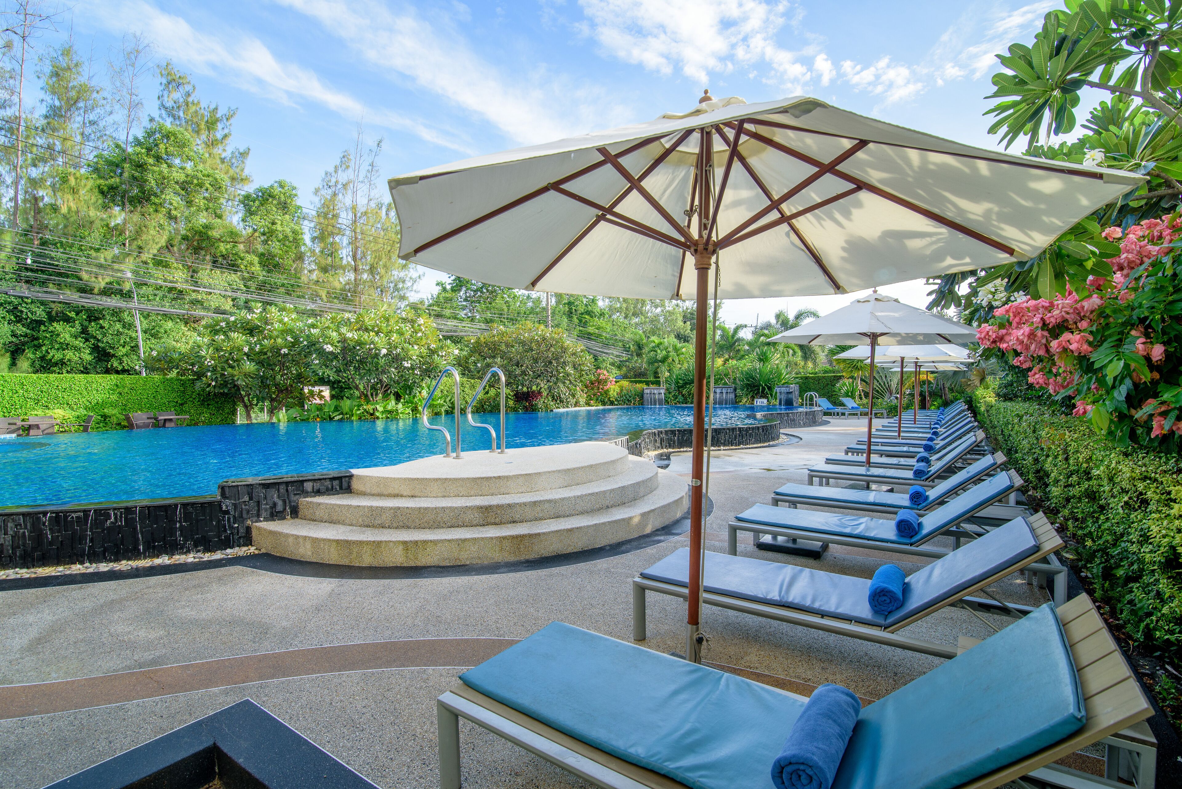 Zona junto a la piscina con sillones de descanso, sombrillas y una escalera de piedra que baja a la piscina.