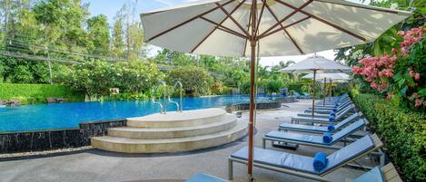 Zona junto a la piscina con sillones de descanso, sombrillas y una escalera de piedra que baja a la piscina.