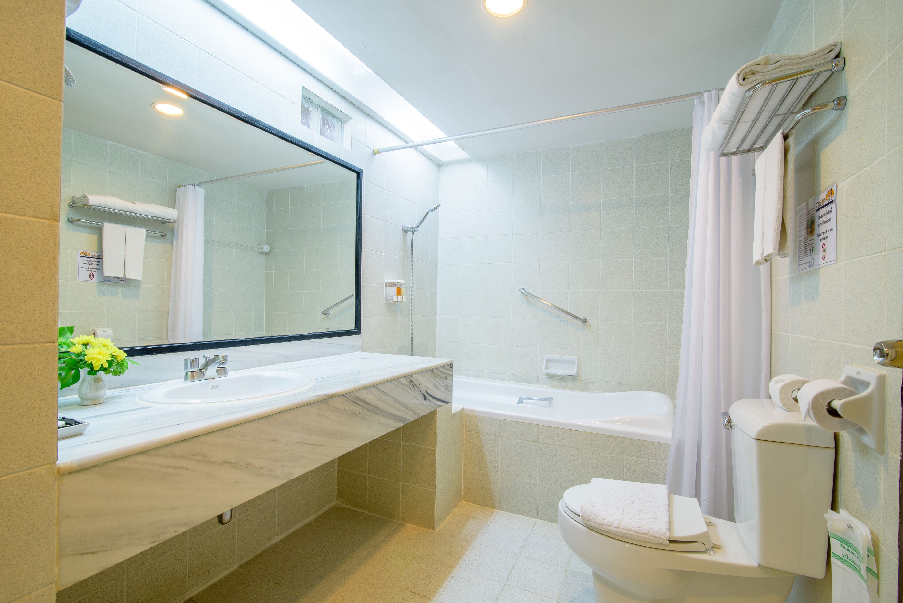 A modern bathroom with a large mirror, a marble sink, a bathtub, and a toilet.