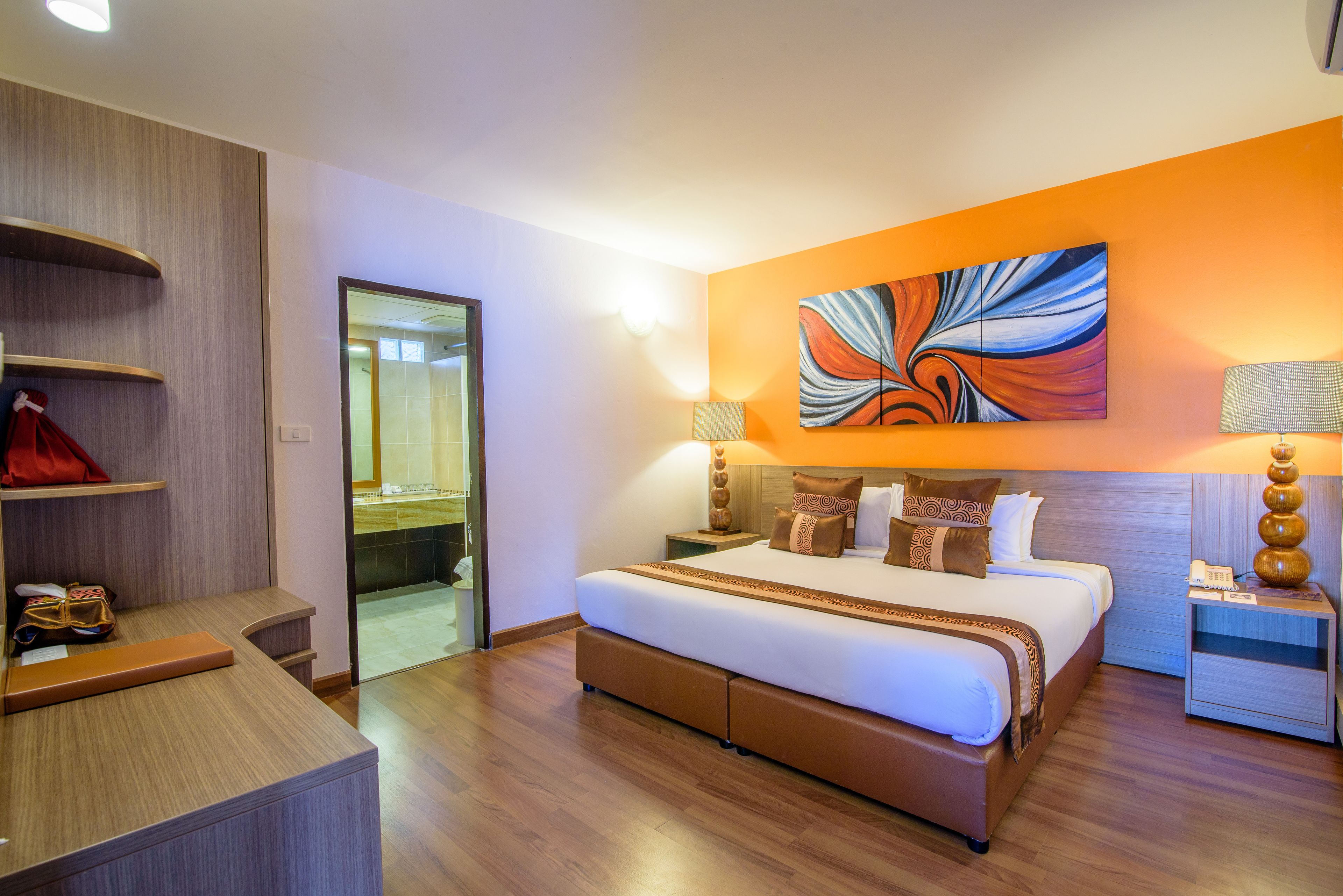 A modern hotel room with a large bed, a wardrobe, a desk, and a bathroom visible through a glass door.