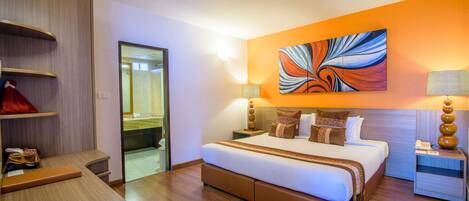 A modern hotel room with a large bed, a wardrobe, a desk, and a bathroom visible through a glass door.