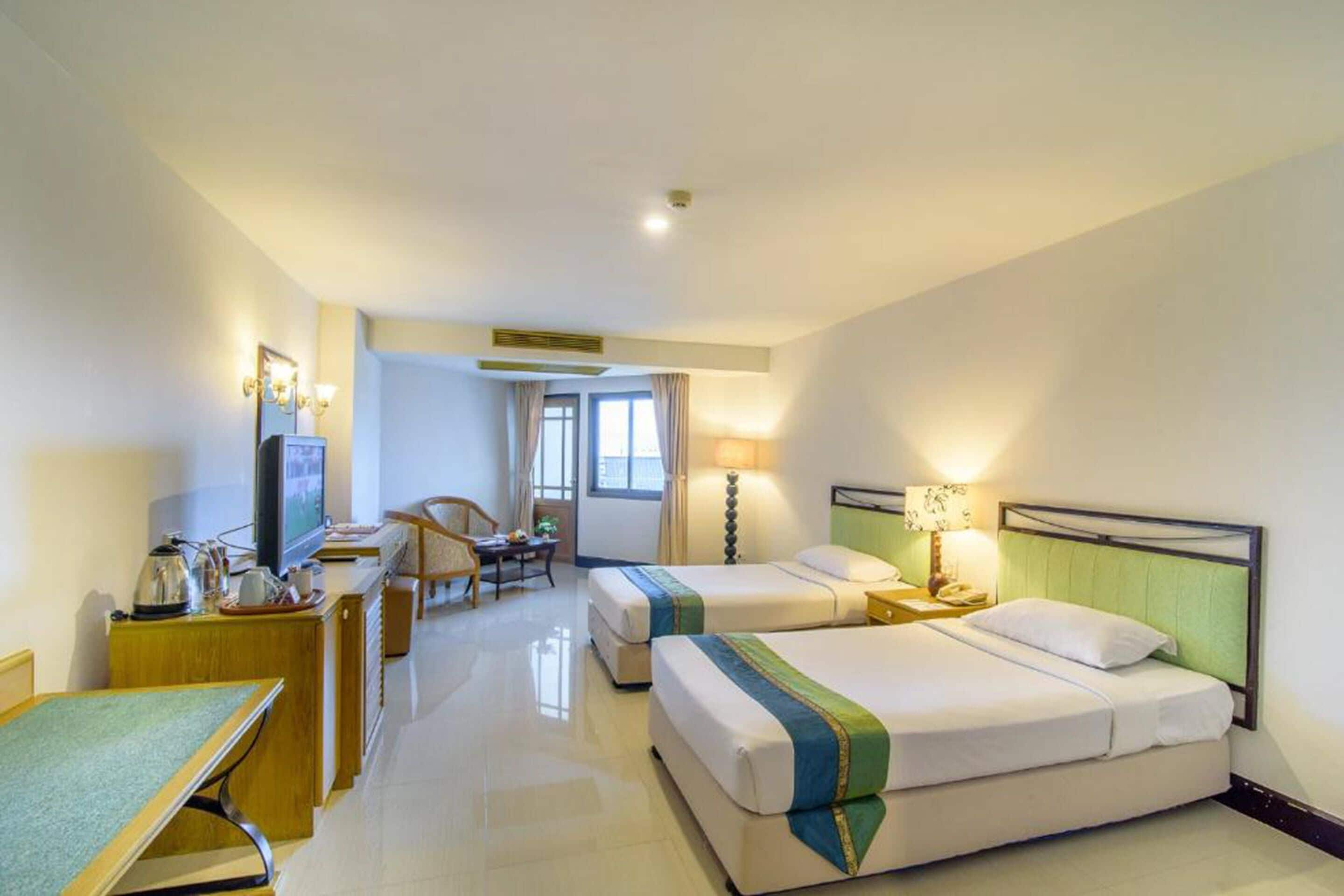 Habitación de hotel con dos camas, un escritorio con silla, televisión y zona de comedor.