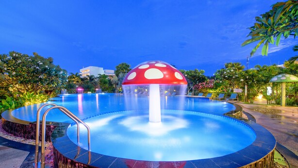 A circular pool with a mushroom-shaped fountain, surrounded by tropical plants and palm trees. - Golden Beach Cha-Am Hotel (Cha-am)