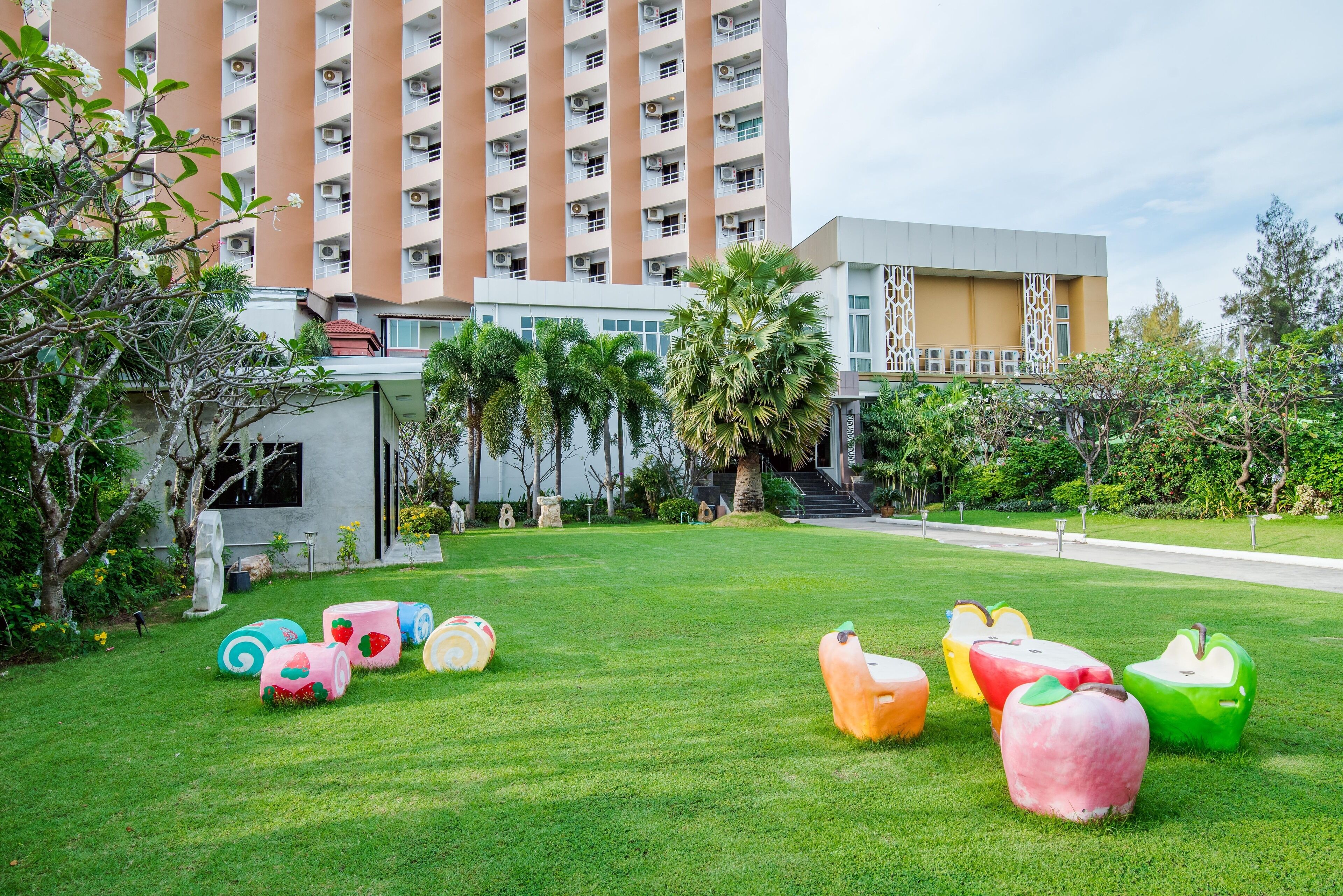 A hotel courtyard with a modern building, palm trees, and colorful apple-shaped planters.