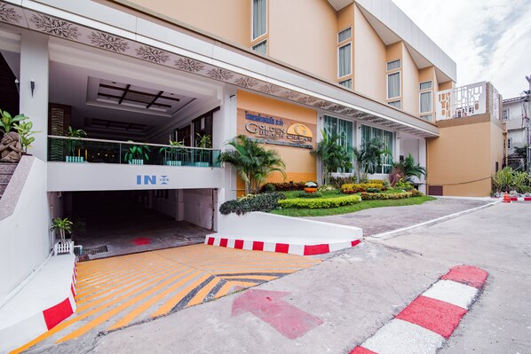 Entrada de hotel con zona cubierta, un cartel que dice 'Golden Berry Garden' y un jardín ajardinado con plantas y un camino.