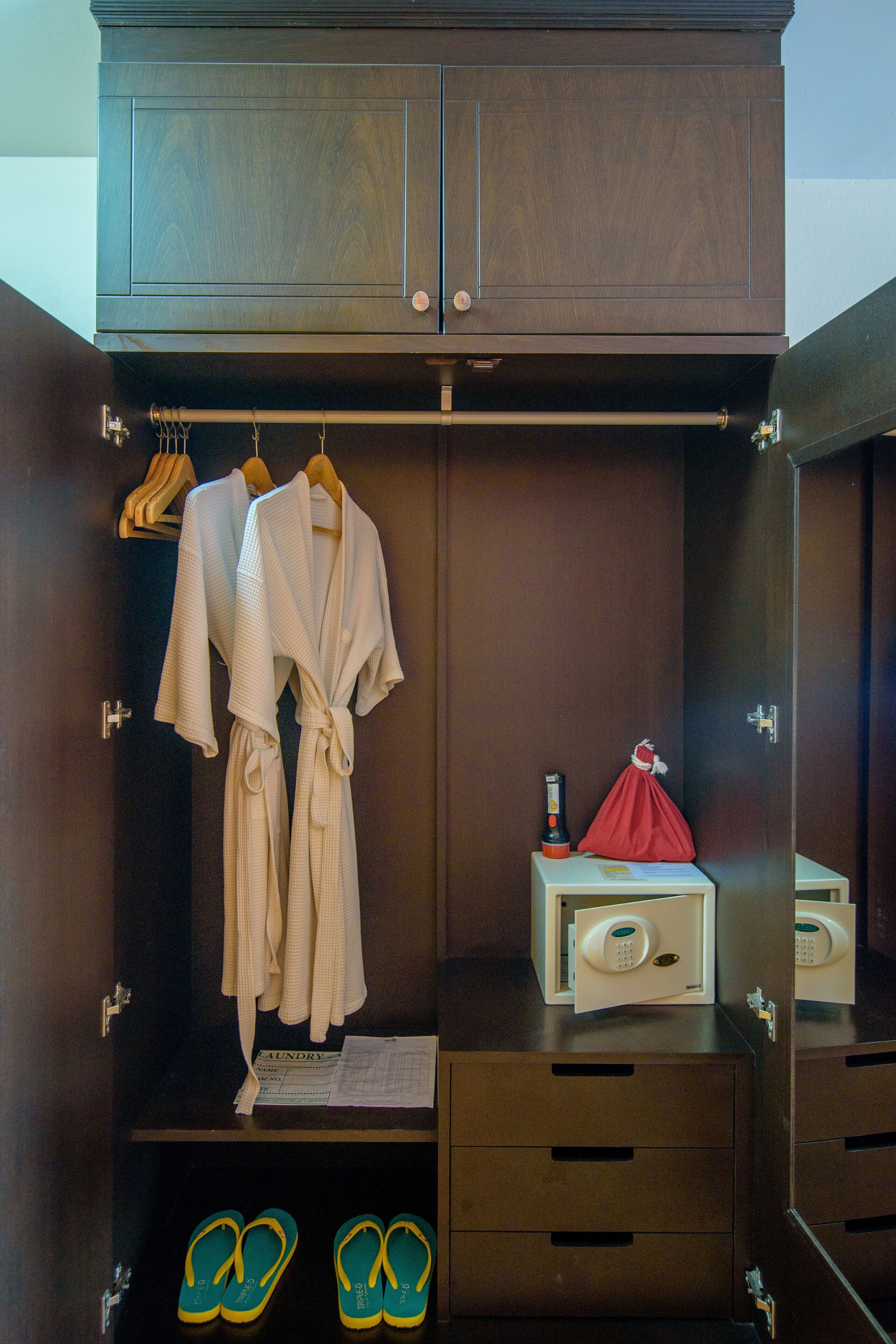 A walk-in closet with hanging robes, a small table with a red bag, and a pair of flip-flops on the floor.