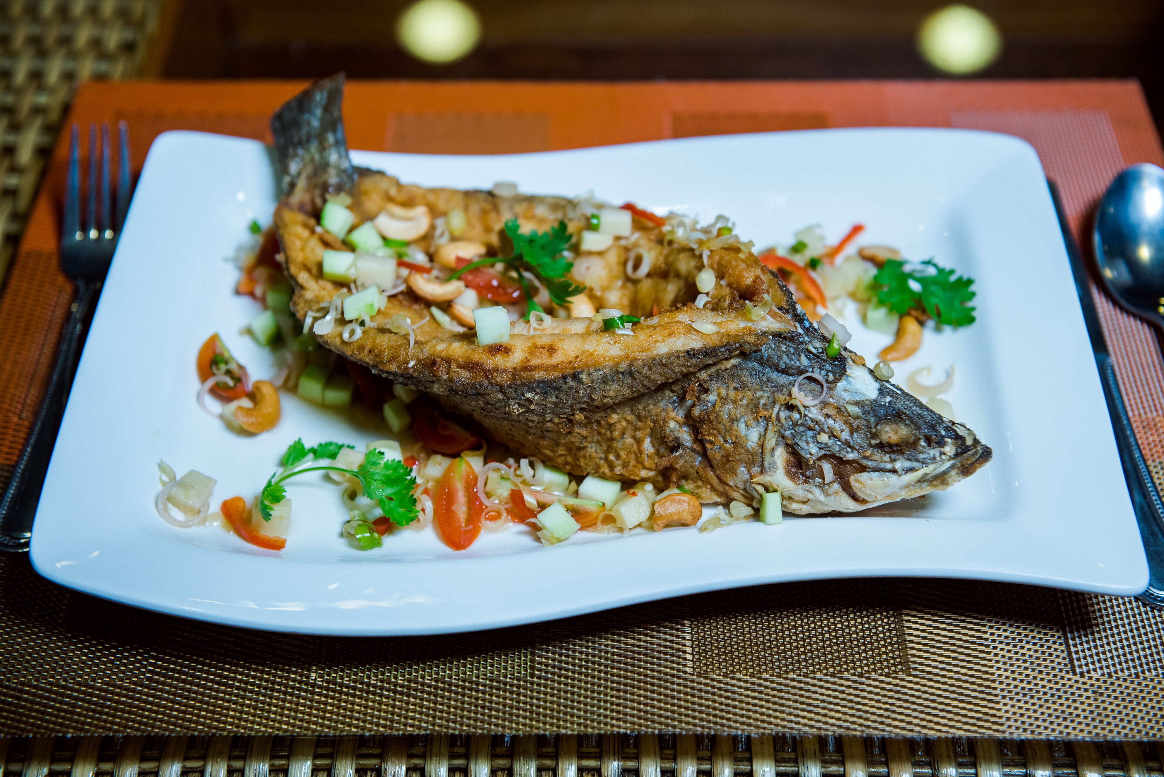 A white plate with a whole fried fish garnished with vegetables and herbs.