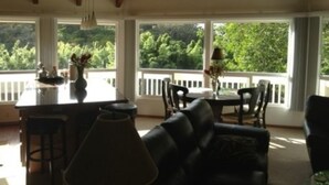 A dining area with a wooden ceiling, large windows, a dining table, chairs, and a bar stool. - Bamboo Valley Inn (Haiku)