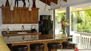 A kitchen with wooden cabinets, a coffee maker, a sink, and a window overlooking greenery. - Bamboo Valley Inn (Haiku)