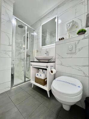 Un baño moderno con cabina de ducha de vidrio, un lavamanos blanco y un inodoro.