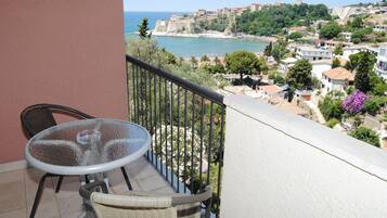 A balcony with a table and chair, overlooking a coastal town with buildings and a sea view.