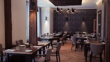A modern dining area with wooden tables and chairs, pendant lighting, and patterned wallpaper.