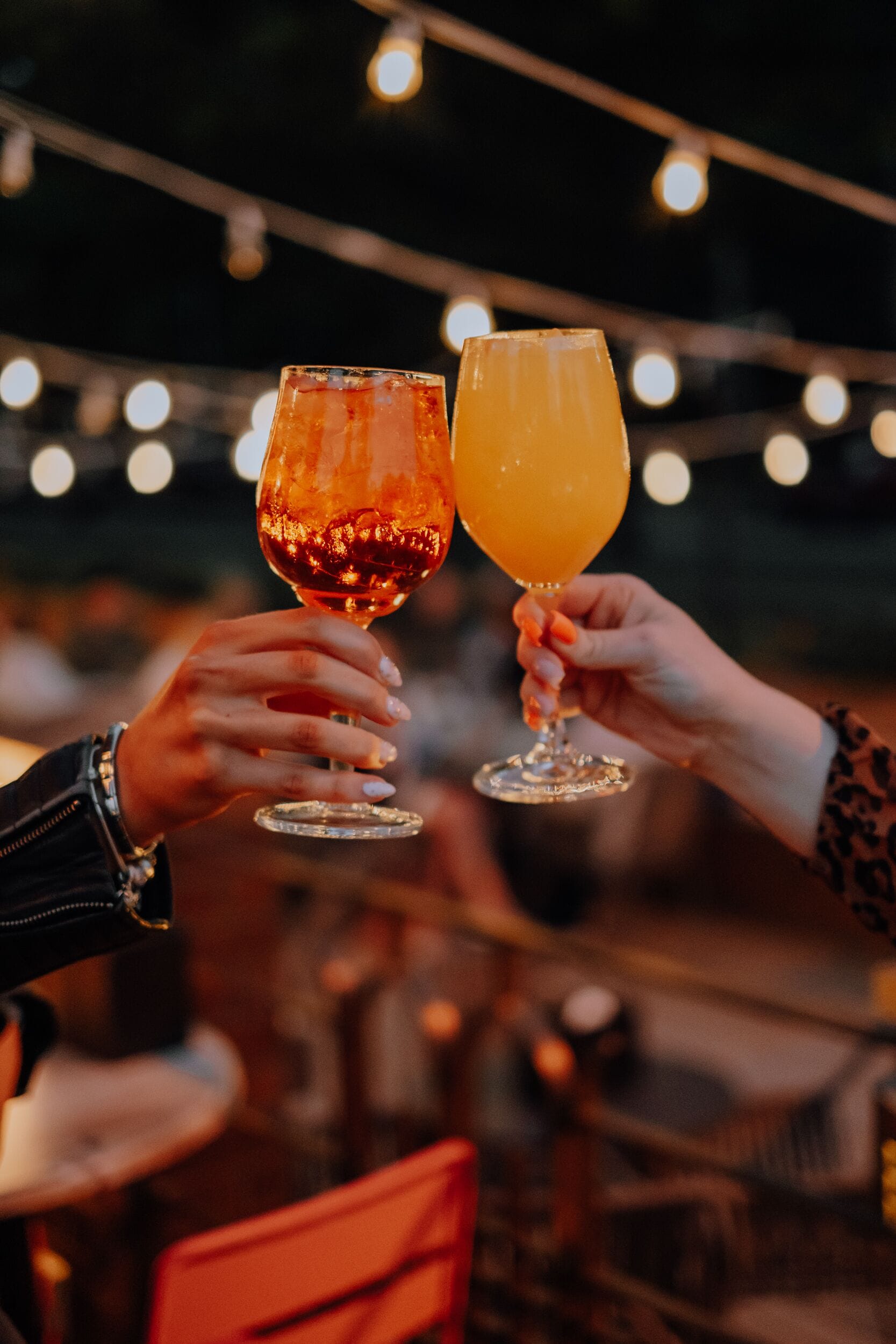 Deux personnes, chacune tenant un verre, sont assises à une table devant laquelle on aperçoit, de façon floue, un arrière-plan illuminé.