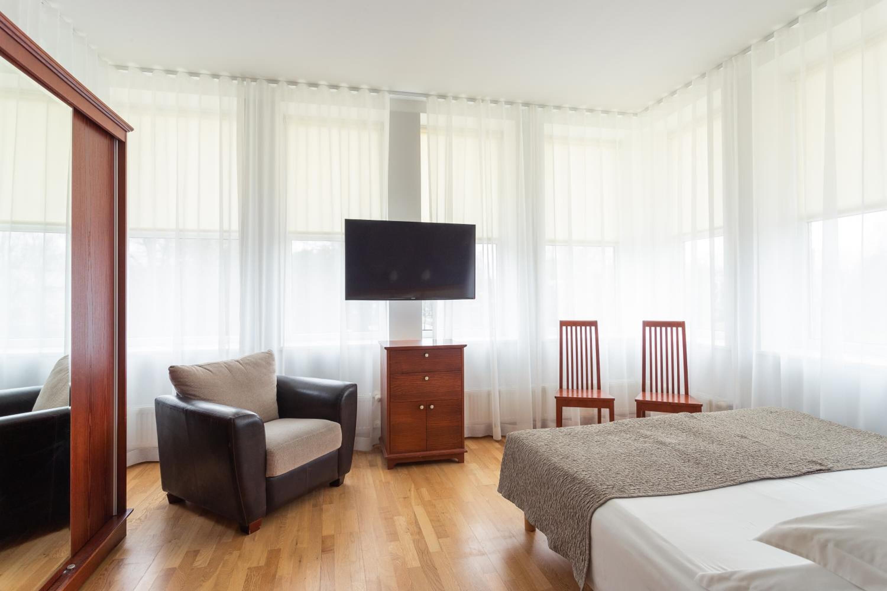 A hotel room with a bed, a chair, a TV, and a wooden cabinet.