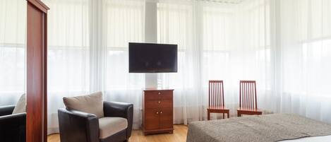 A hotel room with a bed, a chair, a TV, and a wooden cabinet.