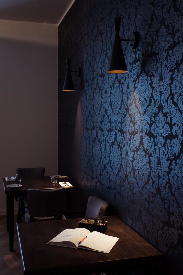 A dimly lit room with a dark wooden table, a chair, and a wall with a blue damask pattern.