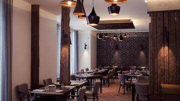 Un restaurante con varias mesas y sillas, iluminación colgante y una pared decorada con papel tapiz estampado.