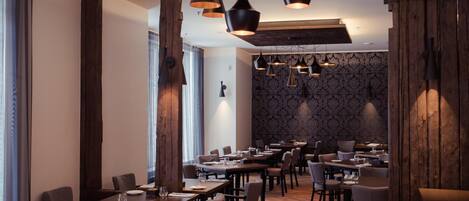 A restaurant with multiple tables and chairs, pendant lighting, and a patterned wallpaper wall.