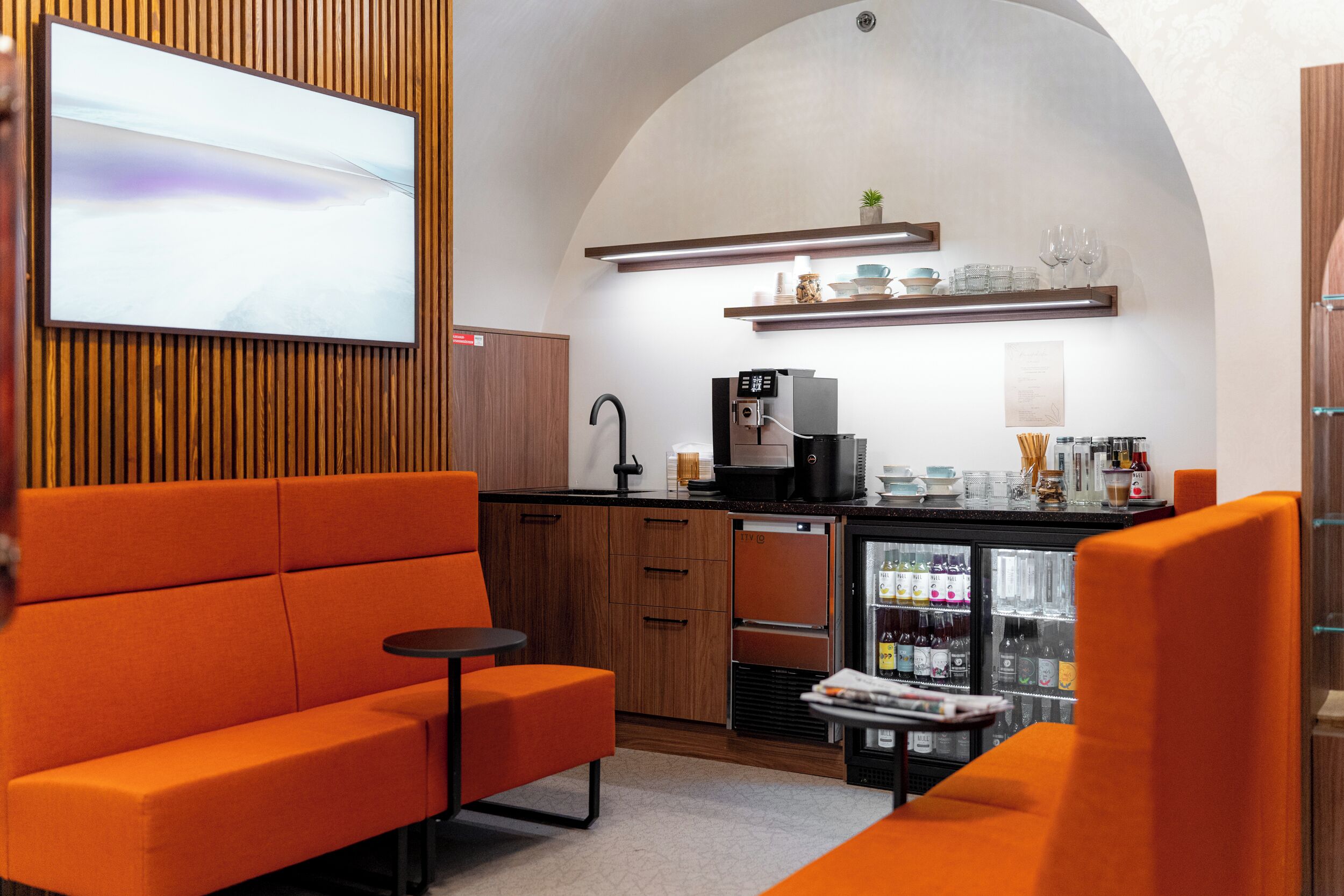 A modern kitchen with a built-in coffee machine, a refrigerator, and a shelf with glassware.