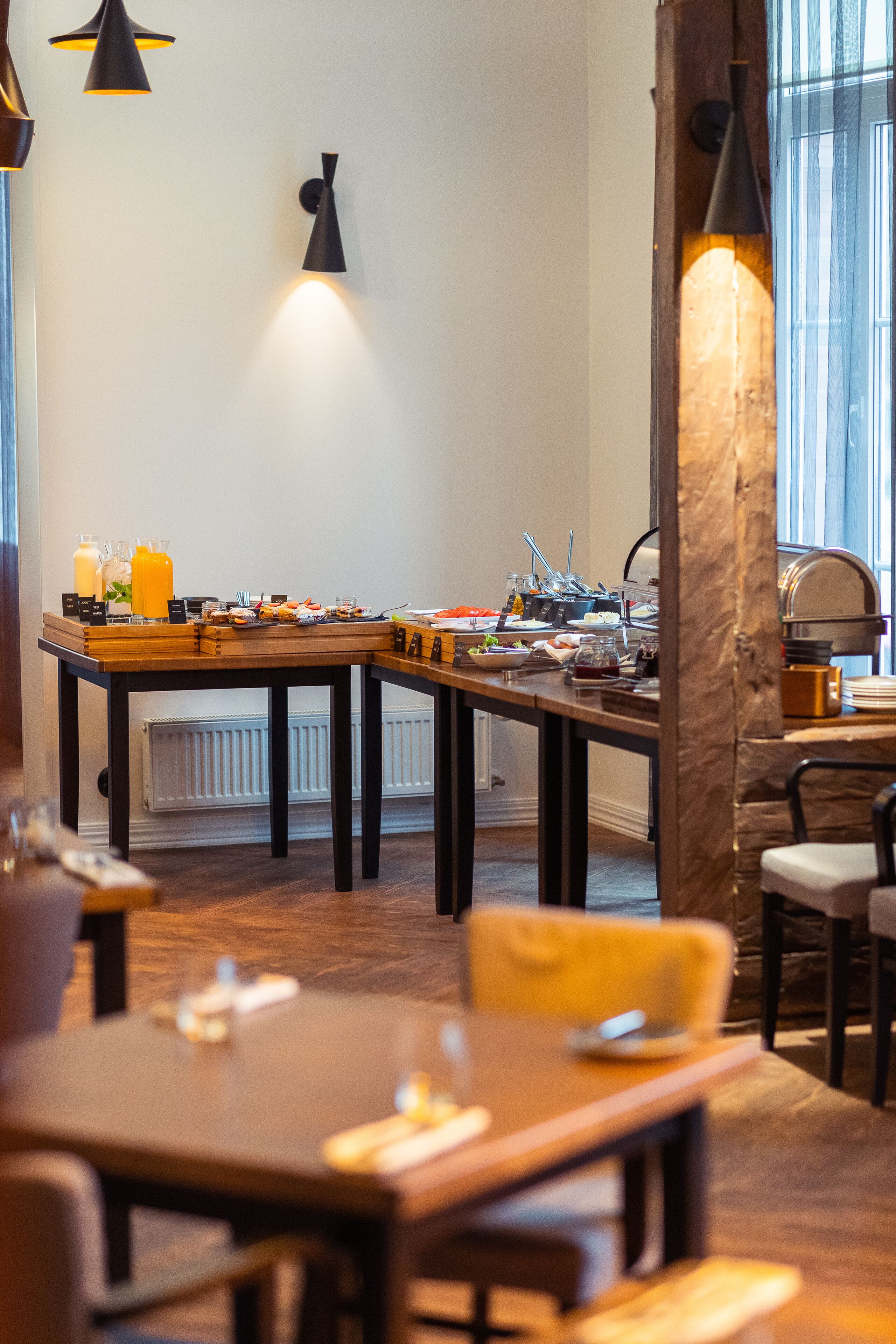 Een eetgedeelte met een lange tafel gedekt voor een maaltijd, een bar met een aanrecht en krukken, en een groot raam dat natuurlijk licht laat binnen.