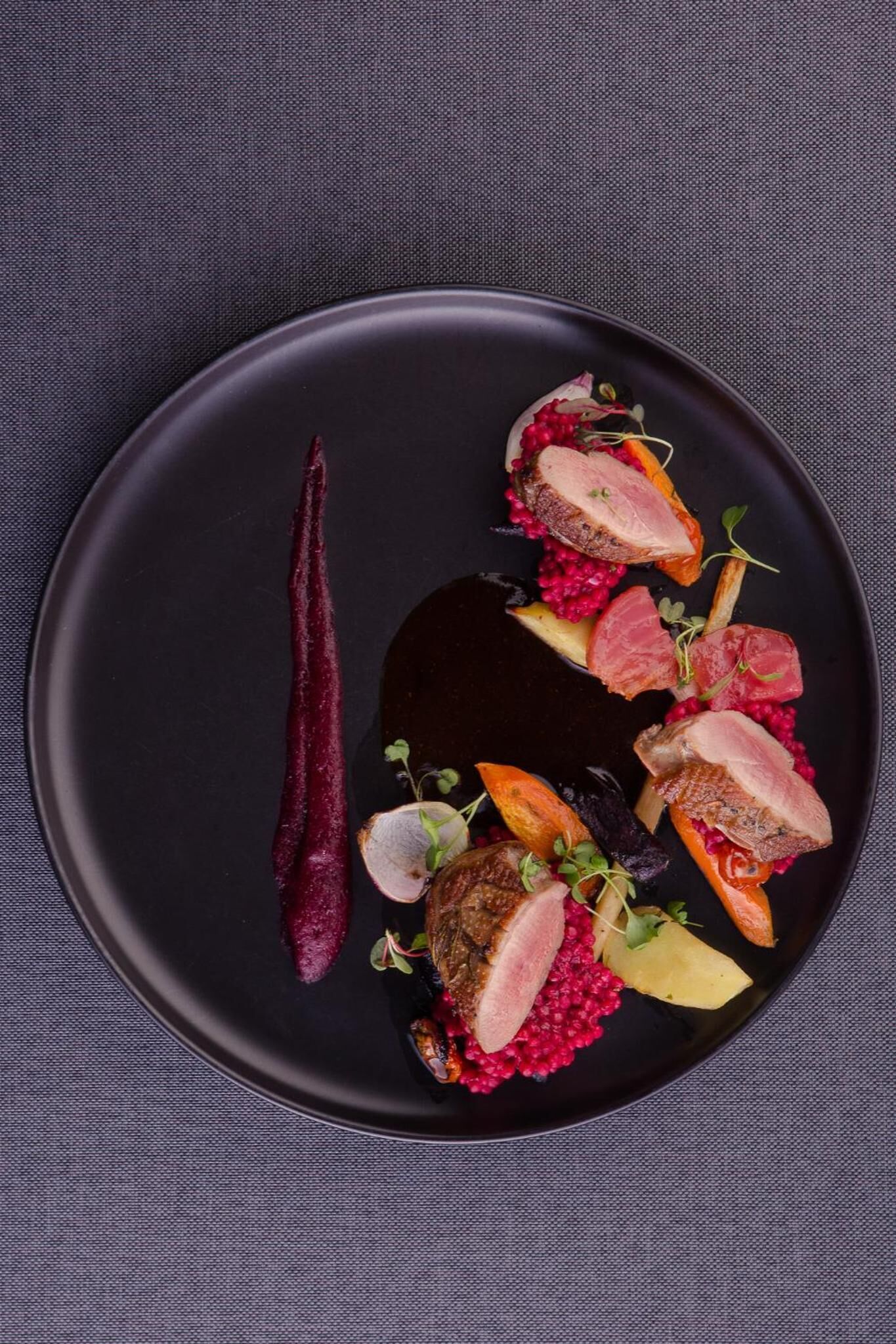 A black plate with a dish of duck, berries, and vegetables.