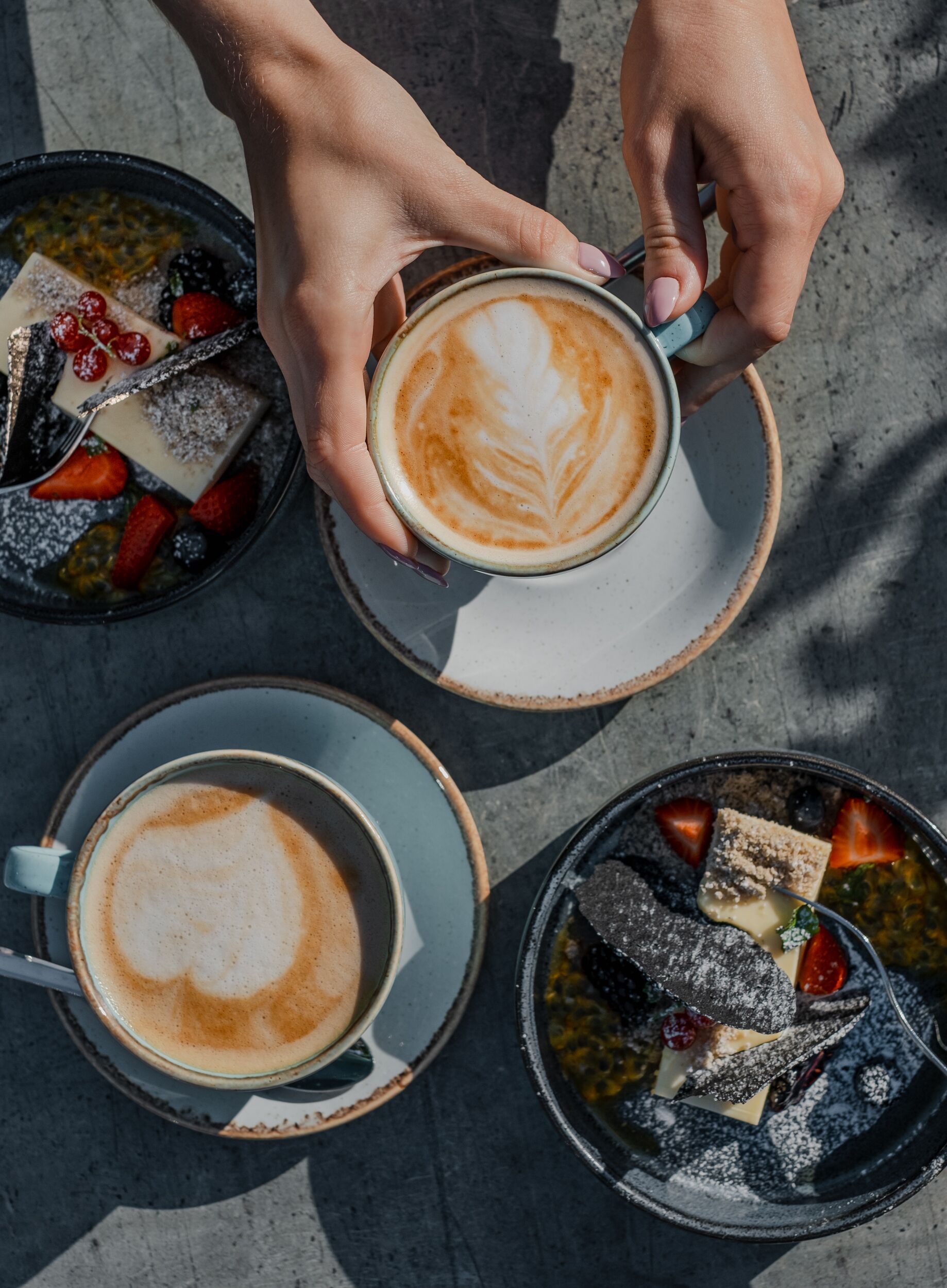Trois tasses de café décorées avec des motifs en latte art, chacune contenant un assortiment différent de fruits et de chocolats.
