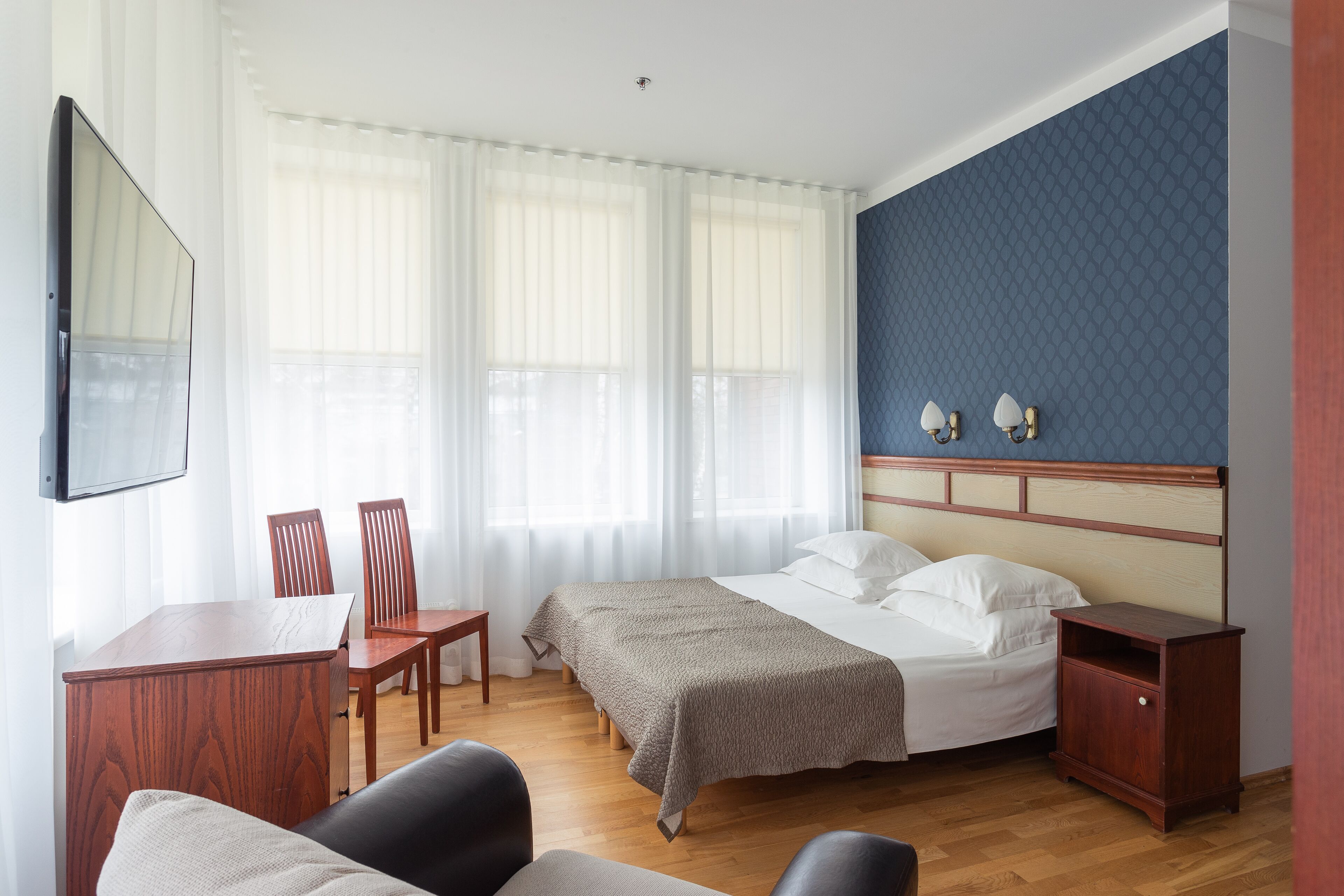 A hotel room with a bed, a desk, two chairs, a TV, and a nightstand.