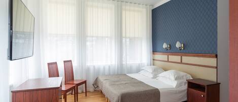 A hotel room with a bed, a desk, two chairs, a TV, and a nightstand.