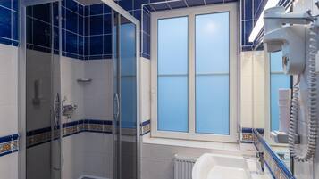A bathroom with a glass-enclosed shower, a white sink, and a mirror with a hairdryer.