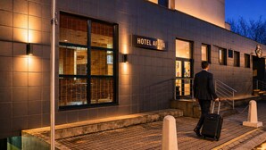A modern hotel exterior with a sign reading 'HOTEL AFRIKA,' a man in a suit with a suitcase, and a security camera. - Afrika Hotel (Frydek-Mistek)