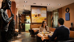 A restaurant with a modern interior, including a dining area with tables and chairs, a large painting on the wall, and a statue on the left. - Afrika Hotel (Frydek-Mistek)