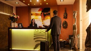 A hotel reception area with a receptionist, a reception desk, a large abstract painting, and decorative masks on the wall. - Afrika Hotel (Frydek-Mistek)