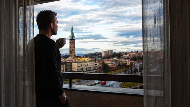 A person standing by a window overlooking a cityscape with a prominent tower and buildings. - Afrika Hotel (Frydek-Mistek)