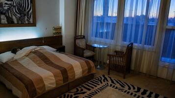 A hotel room with a bed, a chair, a small table, and a zebra-patterned rug.