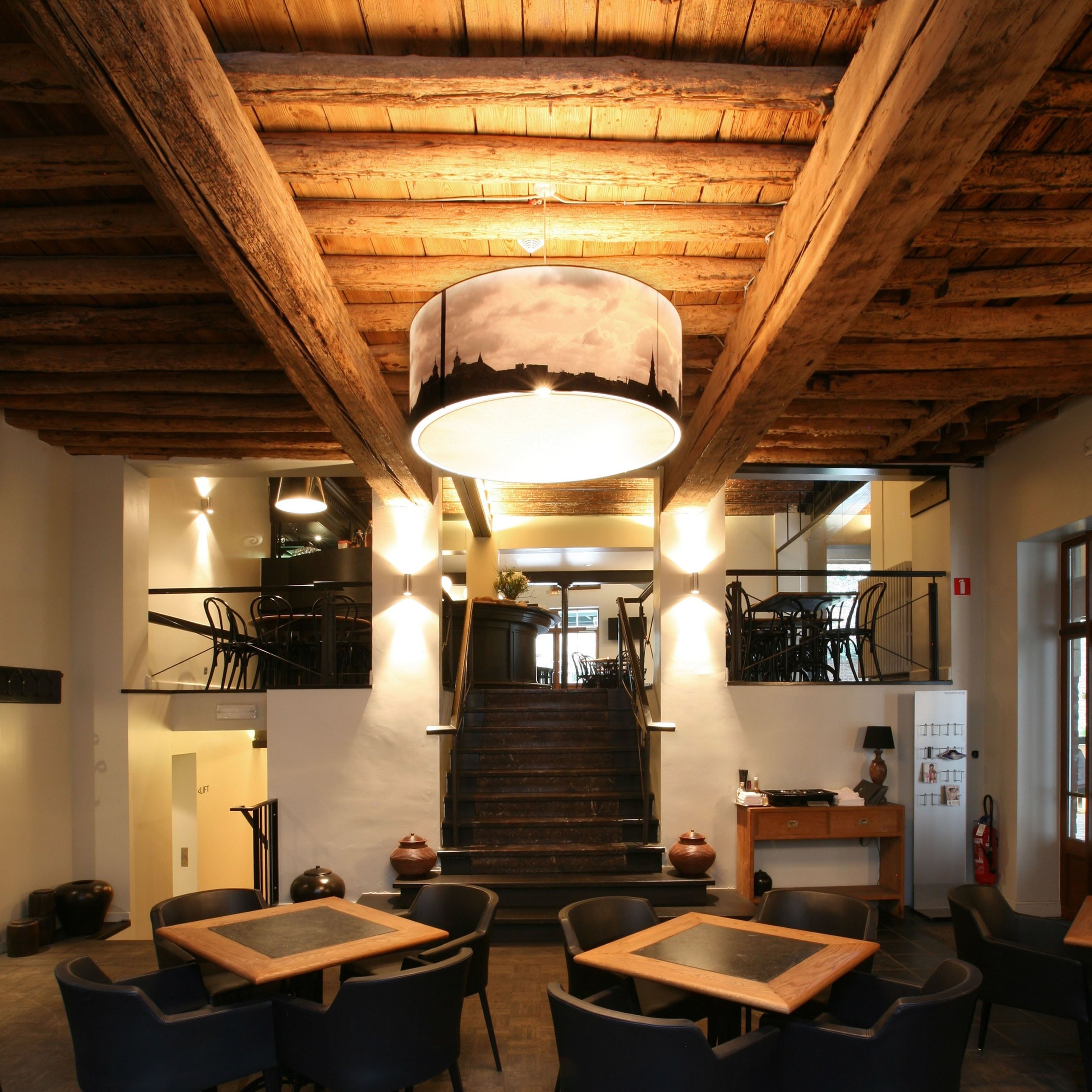 Ein Restaurant mit Holzbalken, einer zentralen Treppe und Tischen mit Stühlen.
