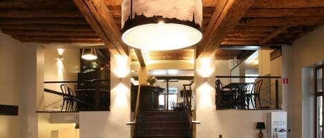Un restaurante con vigas de madera, una escalera central y mesas con sillas.