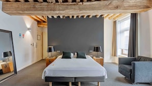 A modern hotel room with a large bed, two bedside tables, a grey sofa, and a wooden ceiling. - Hotel De Groene Hendrickx (Hasselt)