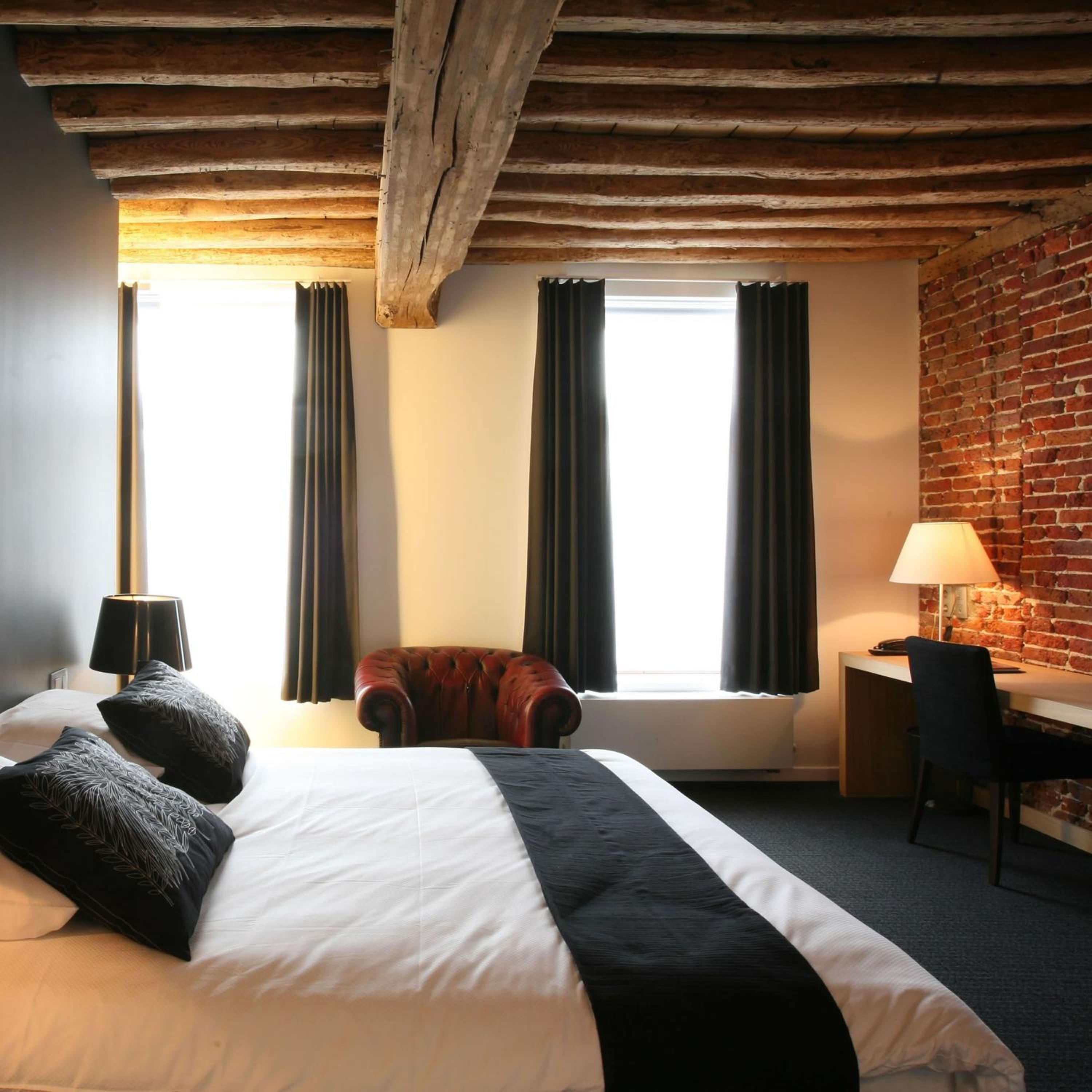 A hotel room with a large bed, a desk, a chair, and a brick wall.