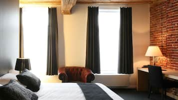 A hotel room with a large bed, a desk, a chair, and a brick wall.