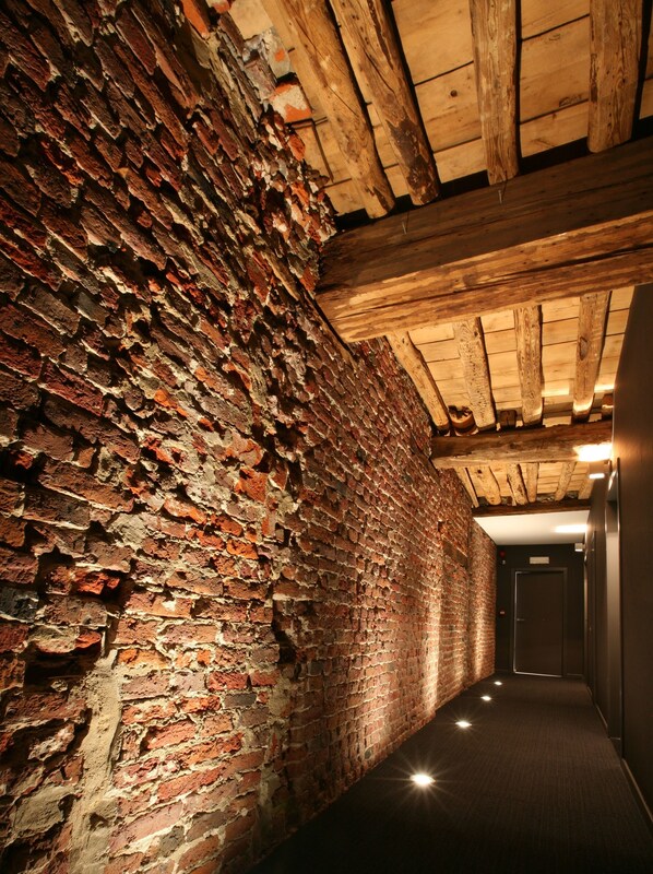 A narrow hallway with exposed brick walls and wooden beams on the ceiling.