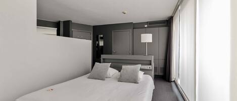 A modern hotel room with a large bed, a bedside table, a lamp, and a view of the city.