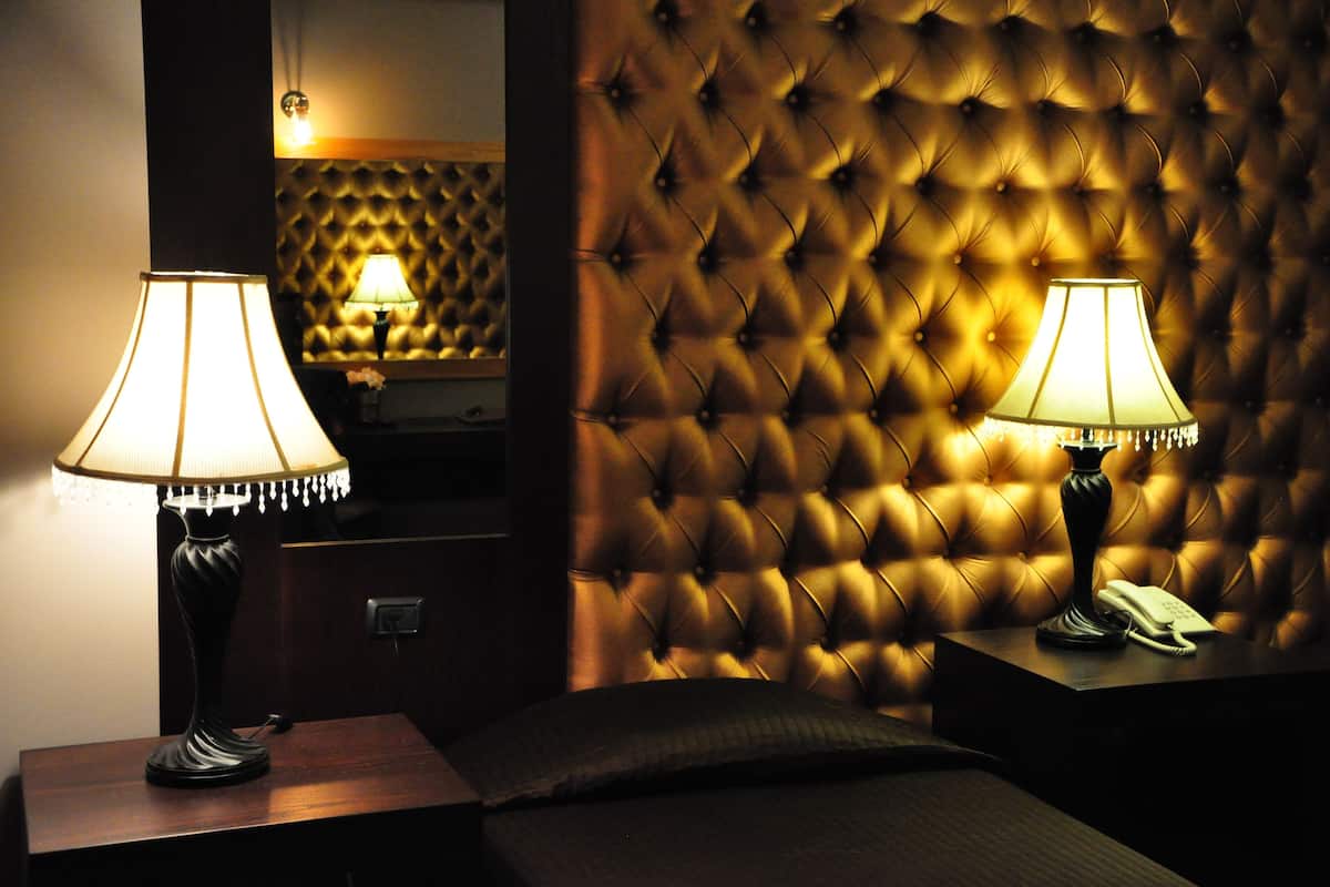 A hotel room with a tufted headboard, two bedside lamps, a bedside telephone, and a mirror reflecting the room's decor.