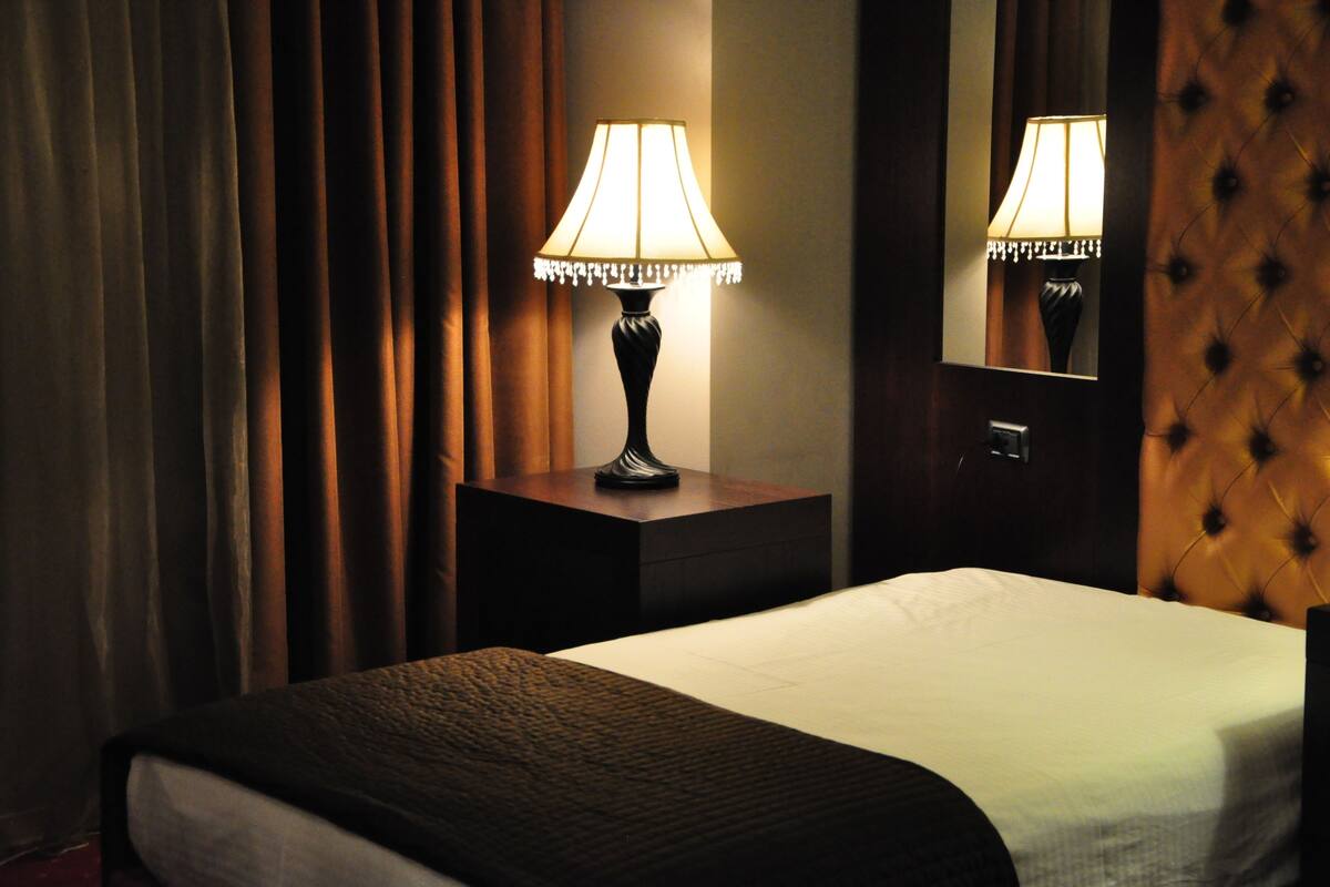 A hotel room with a bed, a nightstand with a lamp, and a mirror.