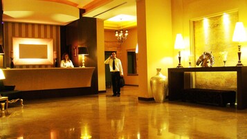 Un vestíbulo de hotel con mostrador de recepción, un candelabro y un jarrón grande.
