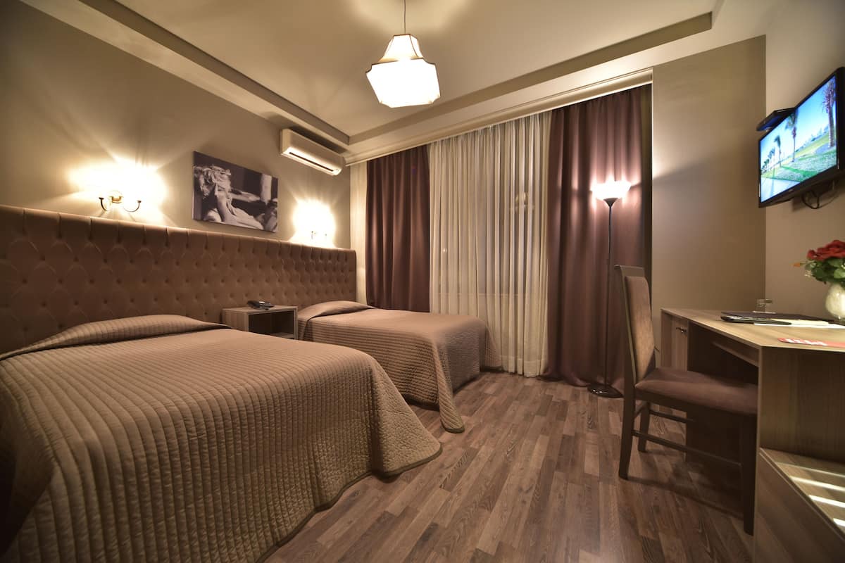 A hotel room with two beds, a desk, a chair, a TV, and a window with curtains.