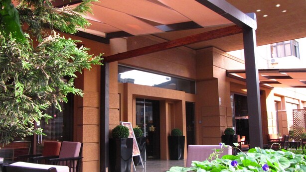 An indoor seating area with tables and chairs, a large potted plant, and a glass door entrance. - Hotel Doro City (Tirana)