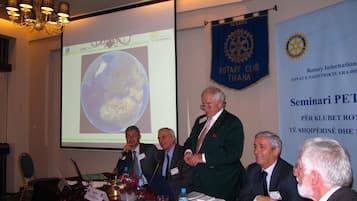 A conference room with a large screen displaying a presentation, a chandelier, and banners for Rotary International.
